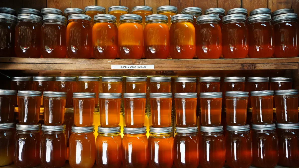 Dozens of honey jars on shelves in a rustic setting create a warm, inviting display.