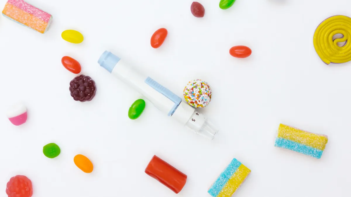 Vibrant assortment of candies surrounding an insulin pen on a white background.